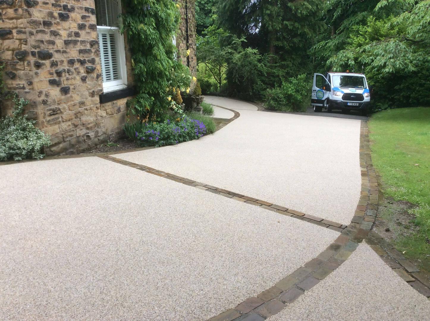 A completed resin driveway beside a stone house and planted border